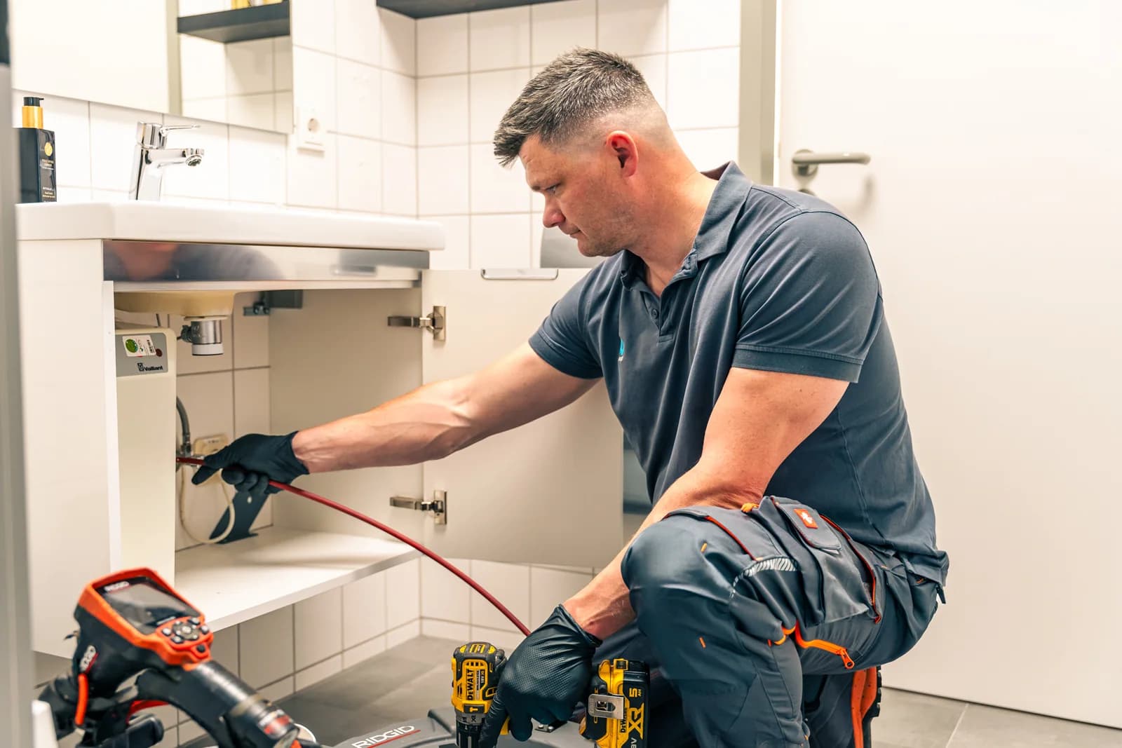 Mitarbeiter der Kaseo GmbH reinigt die Abflussleitung unter einem Waschbecken